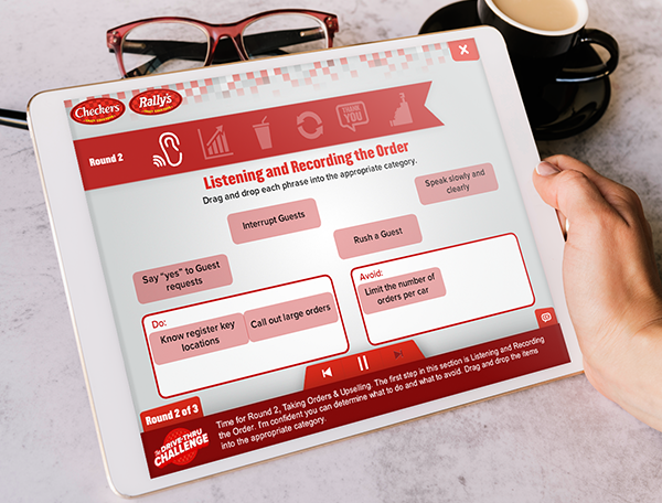 Tablet screen displaying an interactive learning games module for restaurant order taking with a coffee cup and glasses beside it.