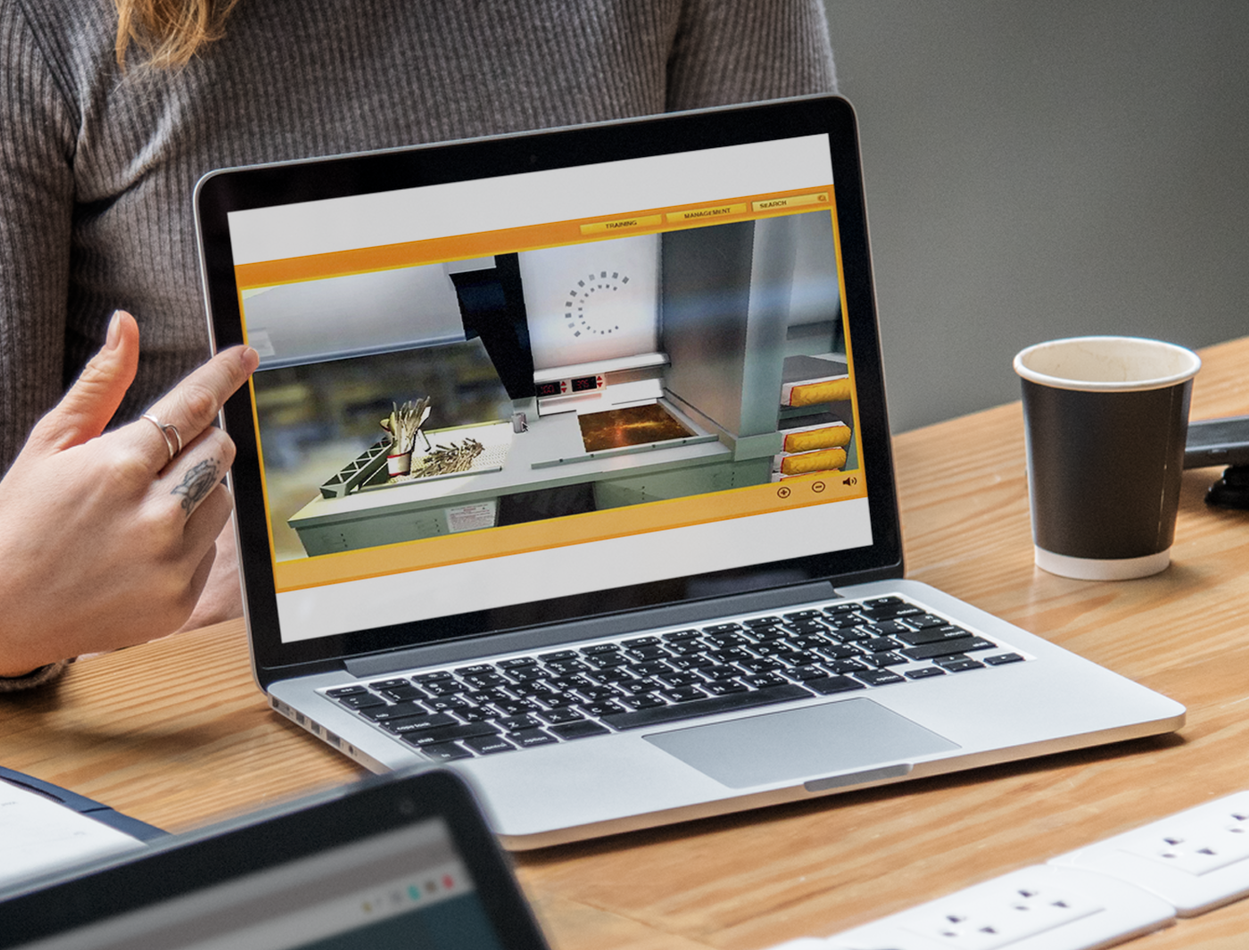 A person pointing at a laptop screen displaying fast food training simulations.