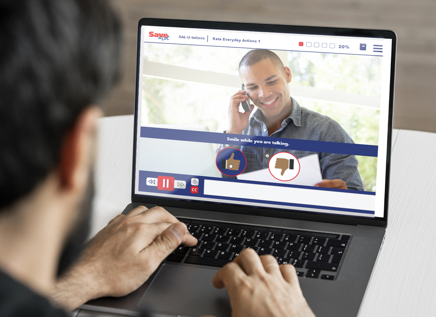 Designing Digitally - A man views an online training video on his laptop featuring a smiling eLearning vendor talking on the phone, with captions and interactive buttons displayed. Designing Digitally -
