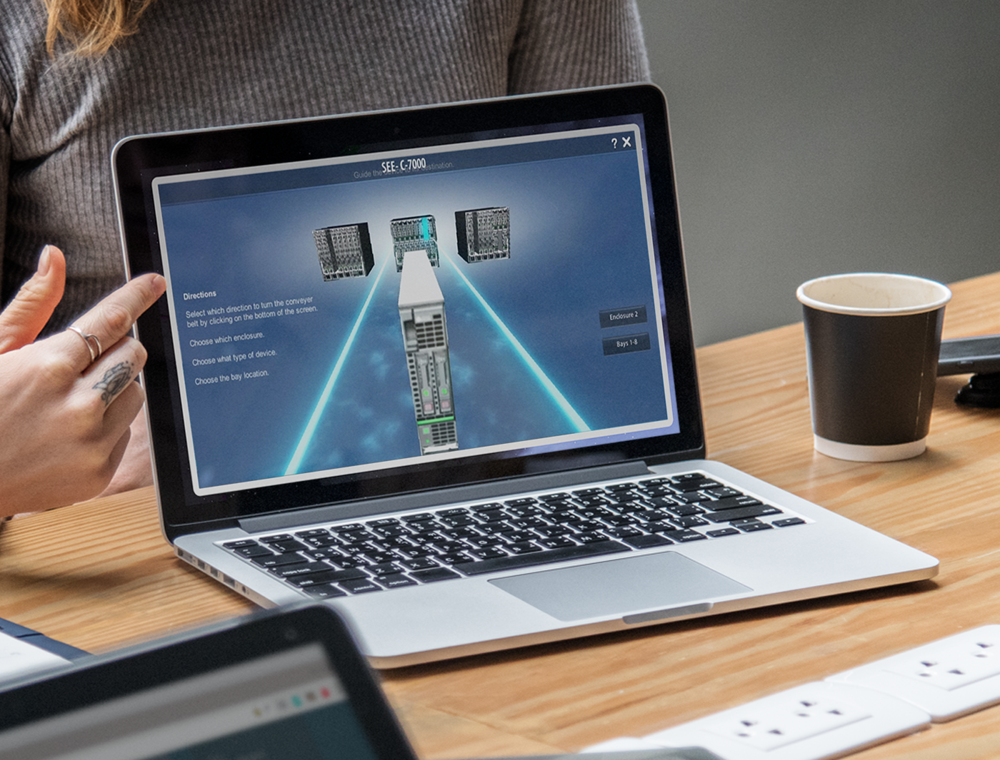 A person is sitting at a table with a laptop displaying a graphic of a server and network connectivity concept during an immersive technical training session while a coffee cup is nearby.