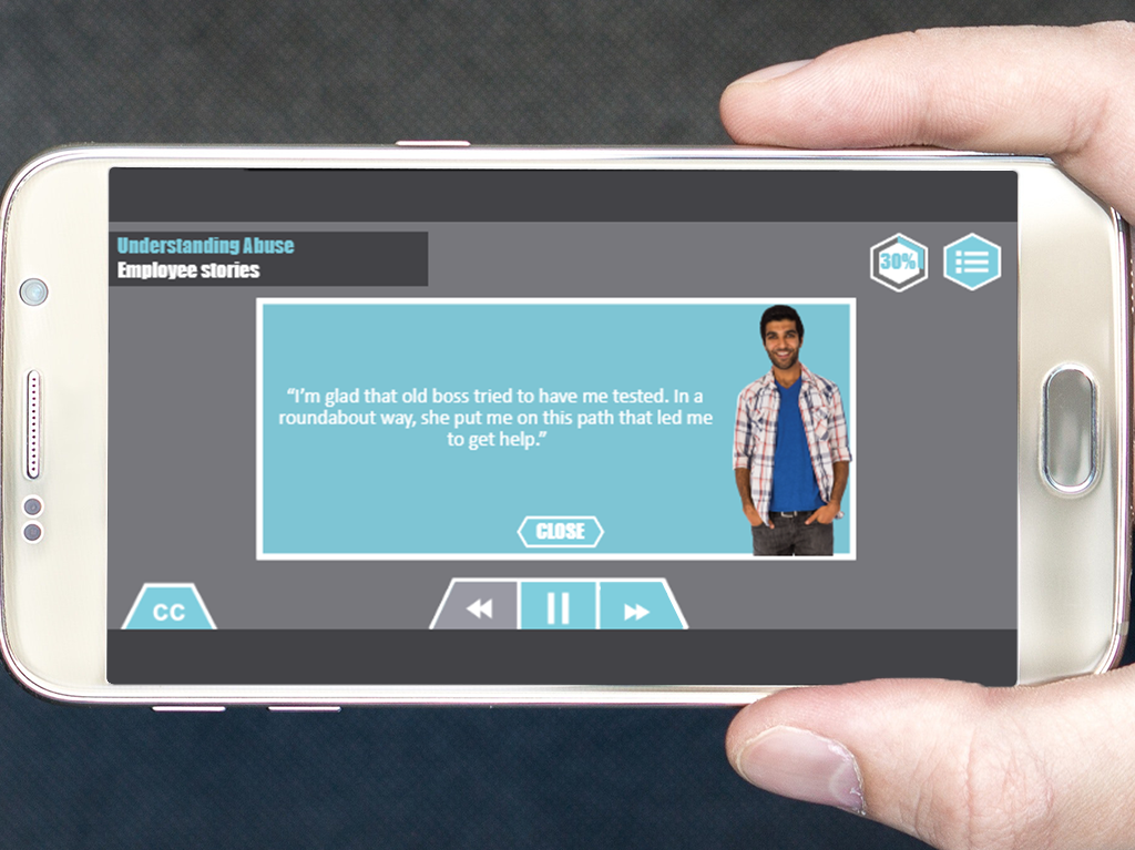 Designing Digitally - A hand holding a smartphone displaying a video titled "Understanding Abuse: Employee Stories," with a man beside a quote about being thankful for guidance towards getting help through the Drug & Alcohol Training Program. Designing Digitally -