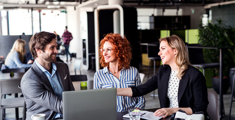 Designing Digitally - Three professionals, two women and one man, are interacting and smiling during a meeting with an eLearning vendor in a modern, brightly lit office space. Designing Digitally -