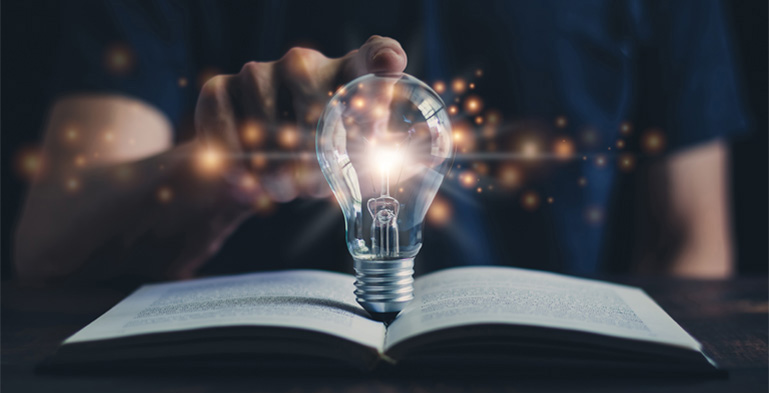 Designing Digitally - A person holding a light bulb over an open book with glowing lights emanating from it, symbolizing ideas and inspiration in the context of virtual reality. Designing Digitally -