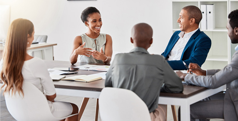 Designing Digitally - A group of five professionals engaging in a lively discussion about mobile app development around a conference table in a bright, modern office. Designing Digitally -