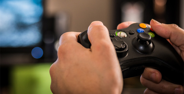 Designing Digitally - Person holding an Xbox controller, focusing on the hands and buttons, with a blurred virtual reality screen in the background. Designing Digitally -