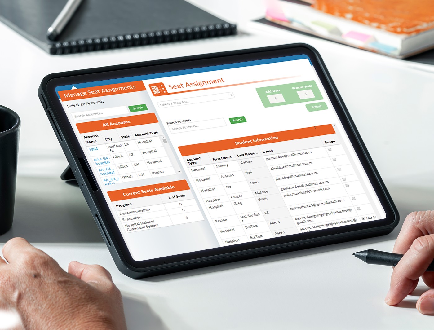 Designing Digitally - A digital tablet displaying a seat assignment management system, showing tables of student names and seat schedules, positioned on a desk in an office setting managed by an eLearning Vendor. Designing Digitally -