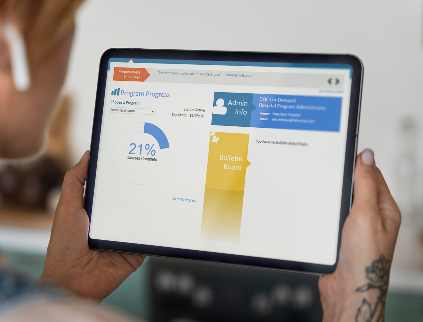 Designing Digitally - Person holding a tablet displaying an eLearning Vendor program progress screen with sections for courses complete, admin info, and bulletin board. Designing Digitally -
