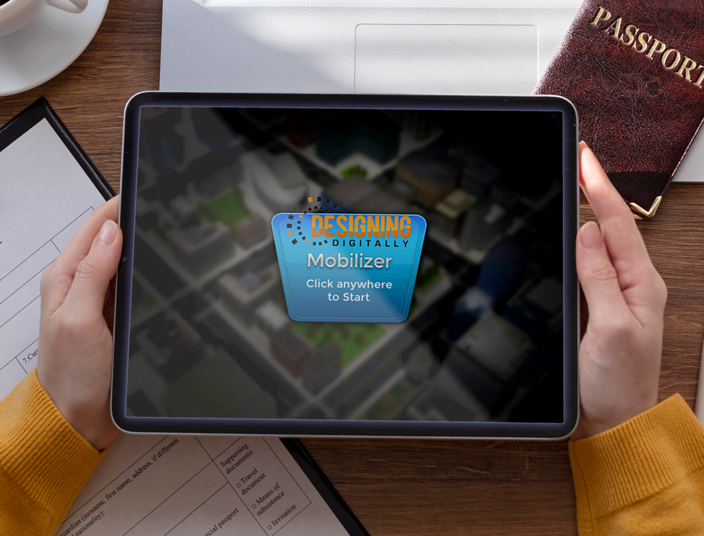 Designing Digitally - Hands holding a tablet displaying a start screen for "eLearning Vendor Designing Digitally Mobilizer" on a desk with documents and a passport. Designing Digitally -