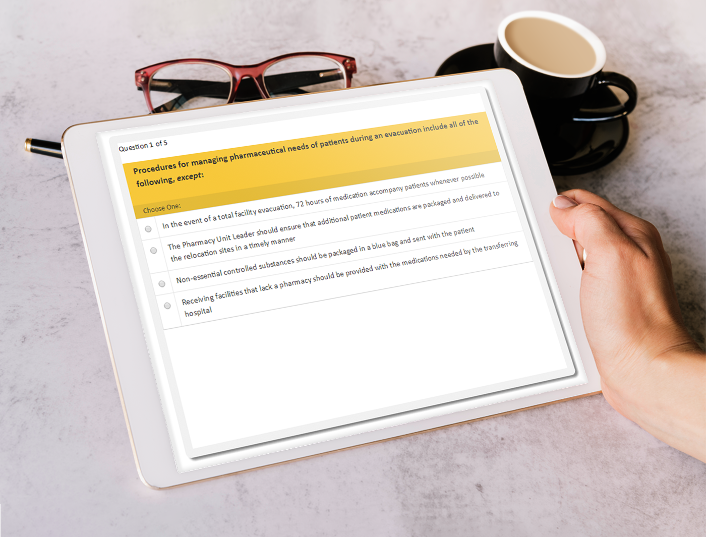 Designing Digitally - A person's hands holding a tablet displaying an online training questionnaire, with glasses and a cup of coffee on the table. Designing Digitally -