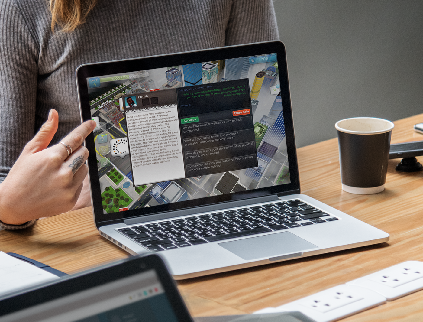 Designing Digitally - A person using a laptop with an eLearning vendor's app showing graphics and text on the screen, with a coffee cup and another laptop nearby on a wooden table. Designing Digitally -