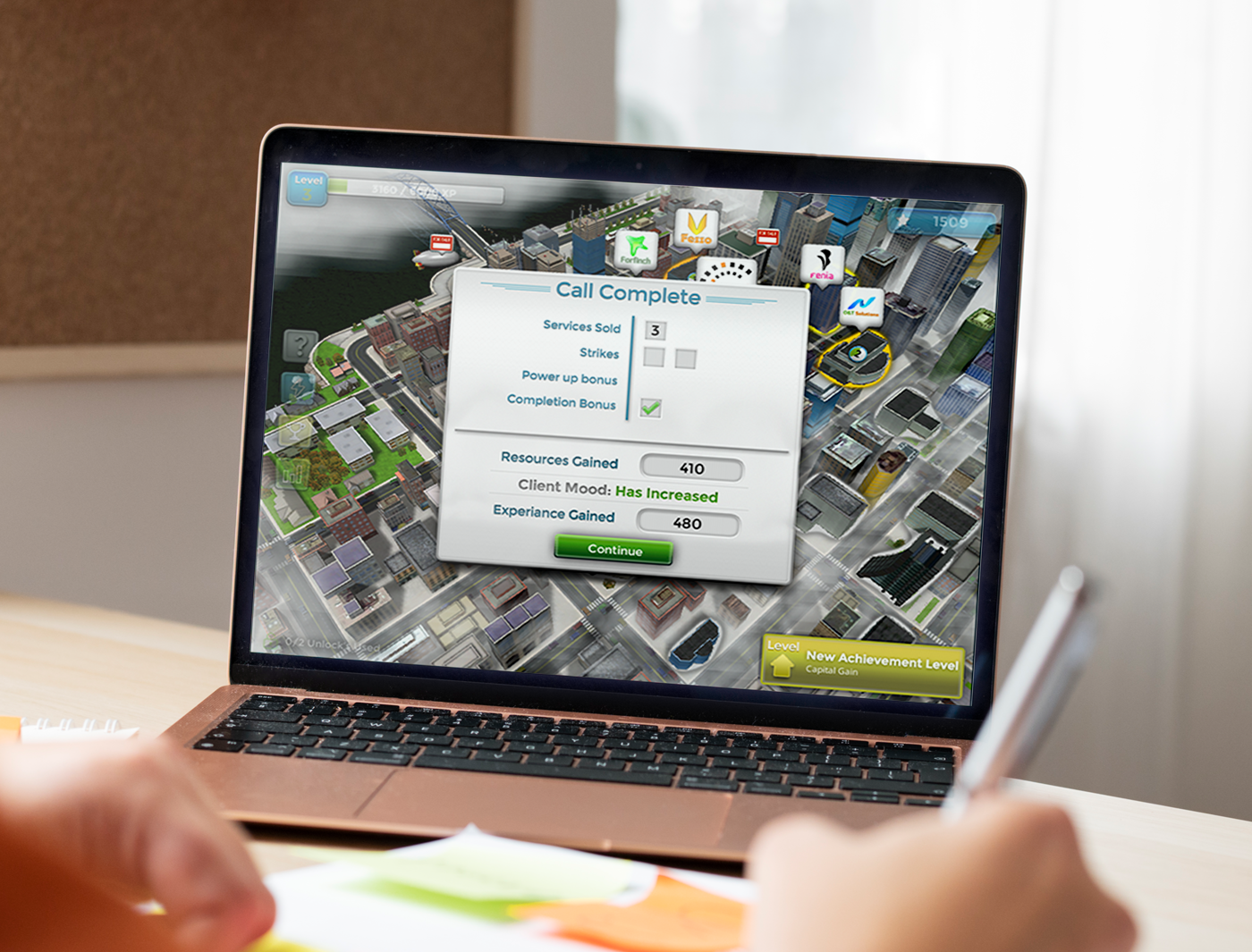 Designing Digitally - A person views a city-building simulation game on a laptop, with the game displaying a "call complete" success message from an eLearning vendor. Designing Digitally -