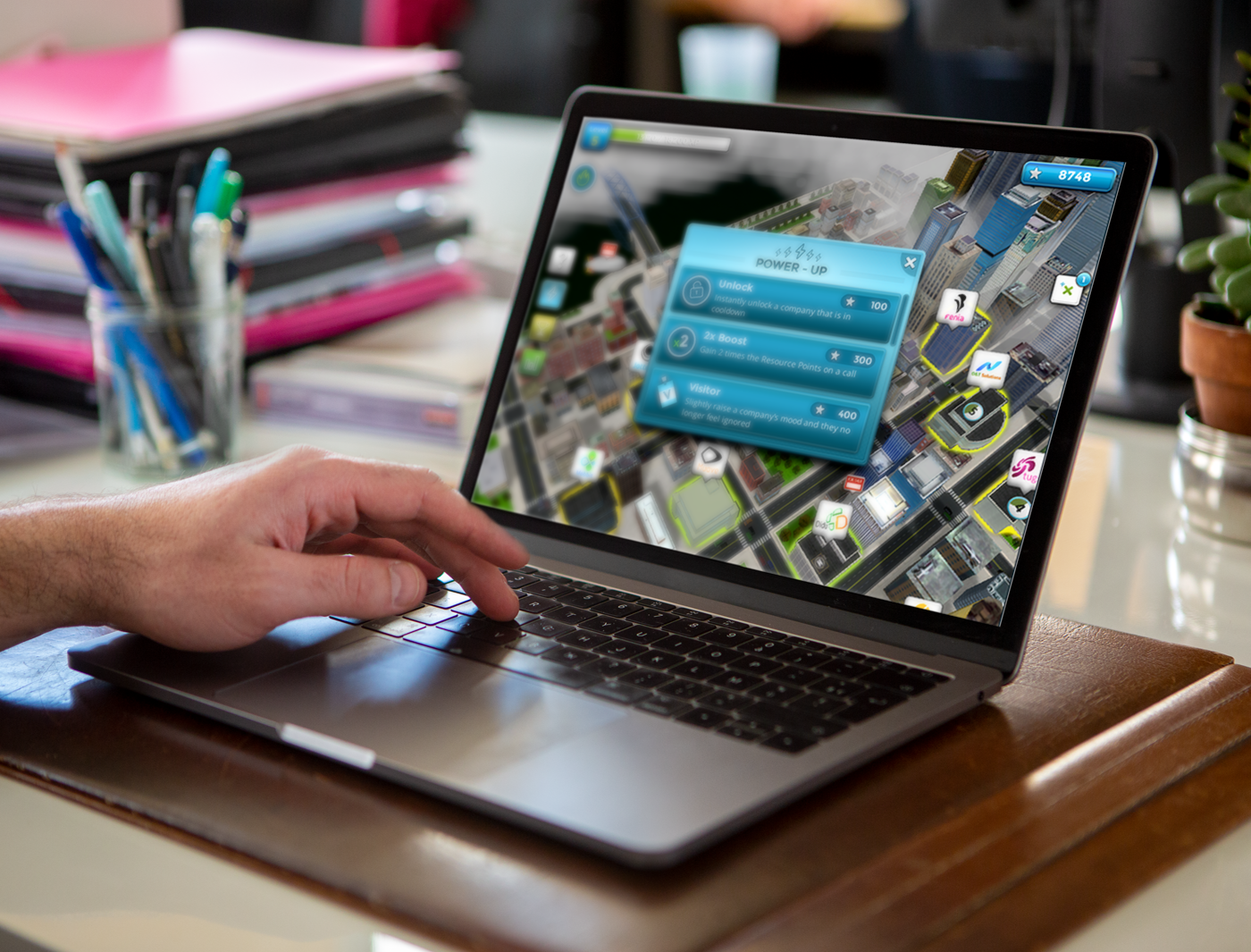 Designing Digitally - A person's hand using a laptop displaying a virtual reality city management simulation game on the screen. Designing Digitally -