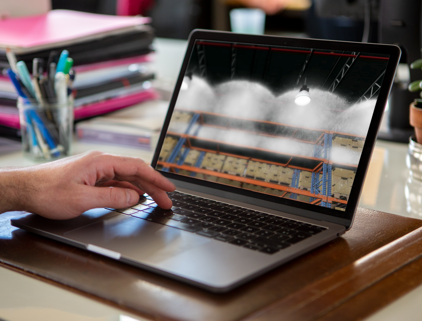 Designing Digitally - A person's hand using a laptop displaying an image of an industrial interior with high ceilings and cargo shelves through an Online Training Vendor platform. Designing Digitally -