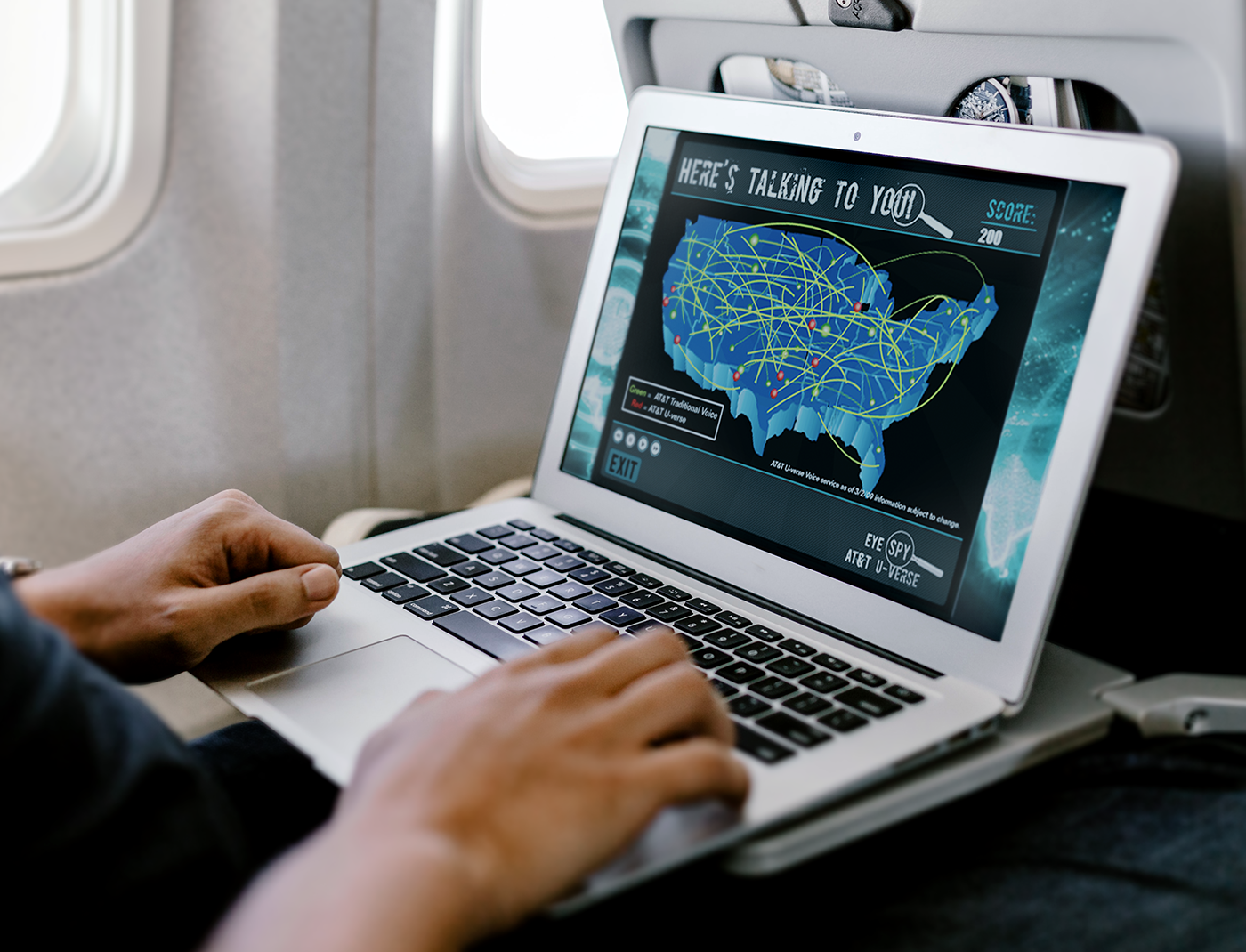 Designing Digitally - A person is using a laptop on an airplane with a U.S. map and lines displayed on the screen, possibly indicating data connections or locations related to trauma nurse training simulations. Designing Digitally -