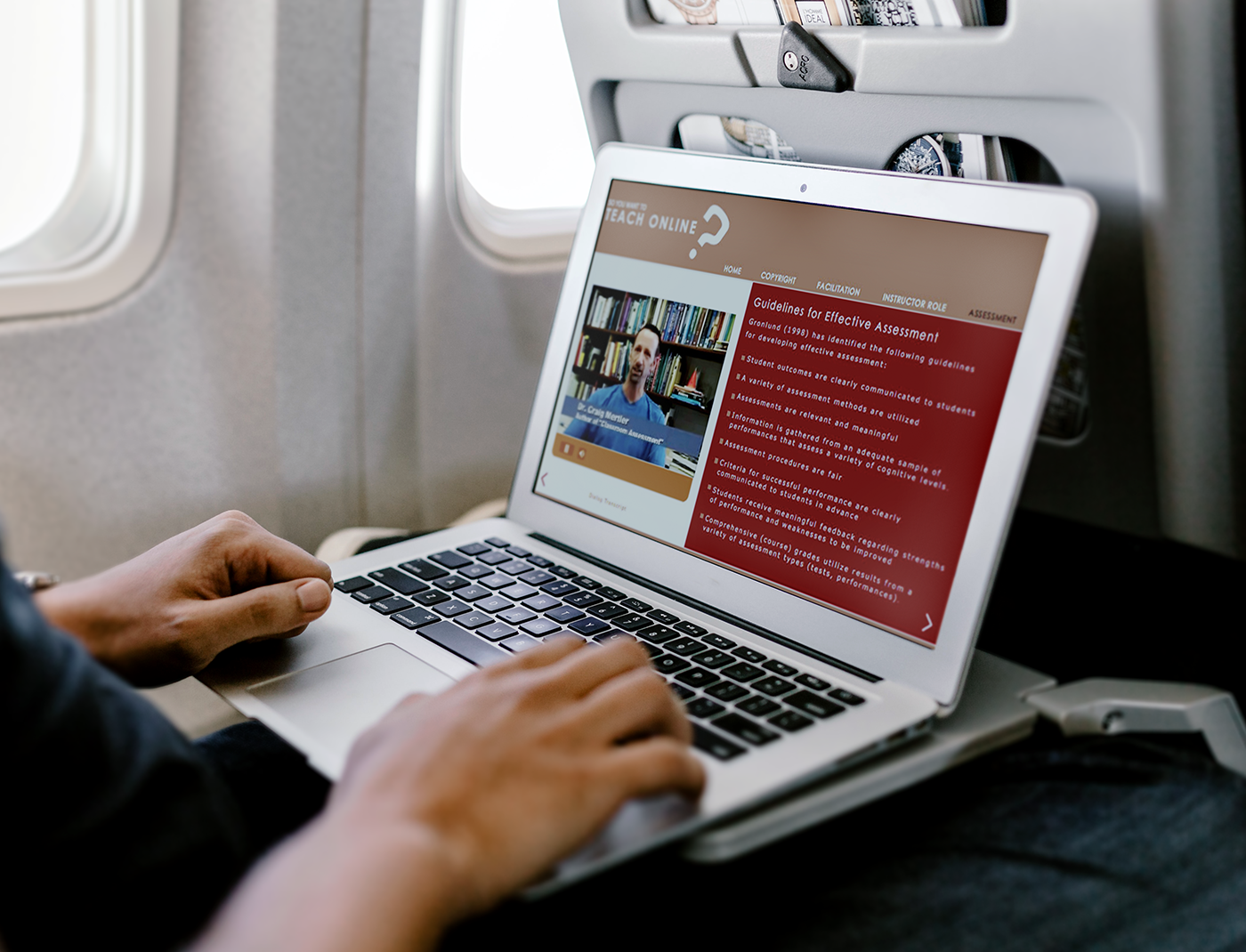 Designing Digitally - Person using a laptop on an airplane, watching an online teaching video on the screen. Designing Digitally -