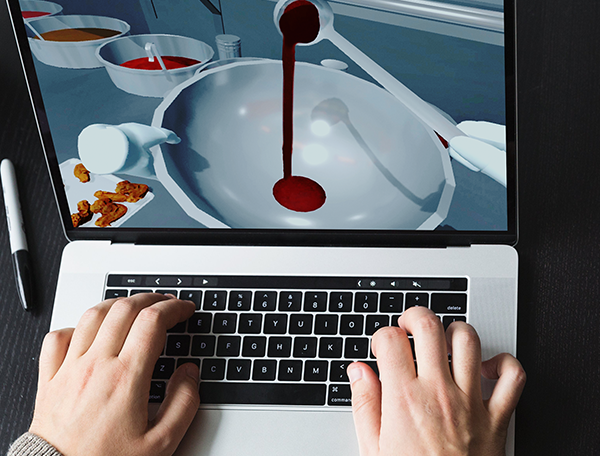 Designing Digitally - Person typing on a laptop showing a cooking simulation game, with a scene of pouring a red liquid into a bowl, ideal for food preparation training. Designing Digitally -