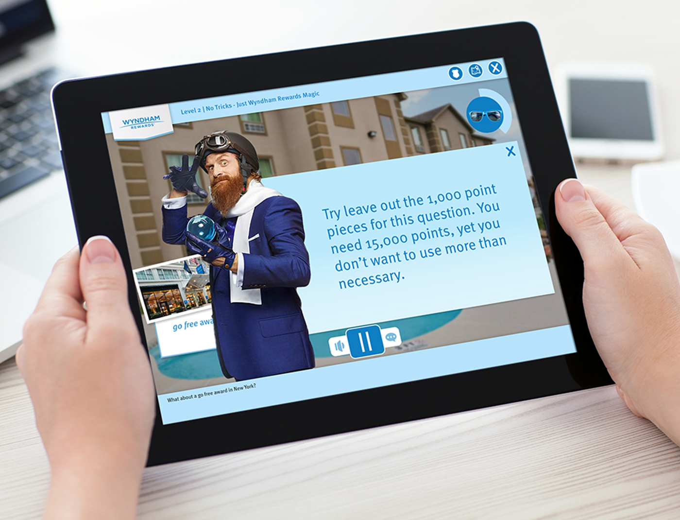 Designing Digitally - Person holding a tablet showing a game with a cartoon character saying, "Try leaving out the 1,000 point pieces for this question. You need 15,000 points, yet you don't want to use more than necessary." This could be part of the Customer Rewards Training Program for Wyndham Hotels. Designing Digitally -
