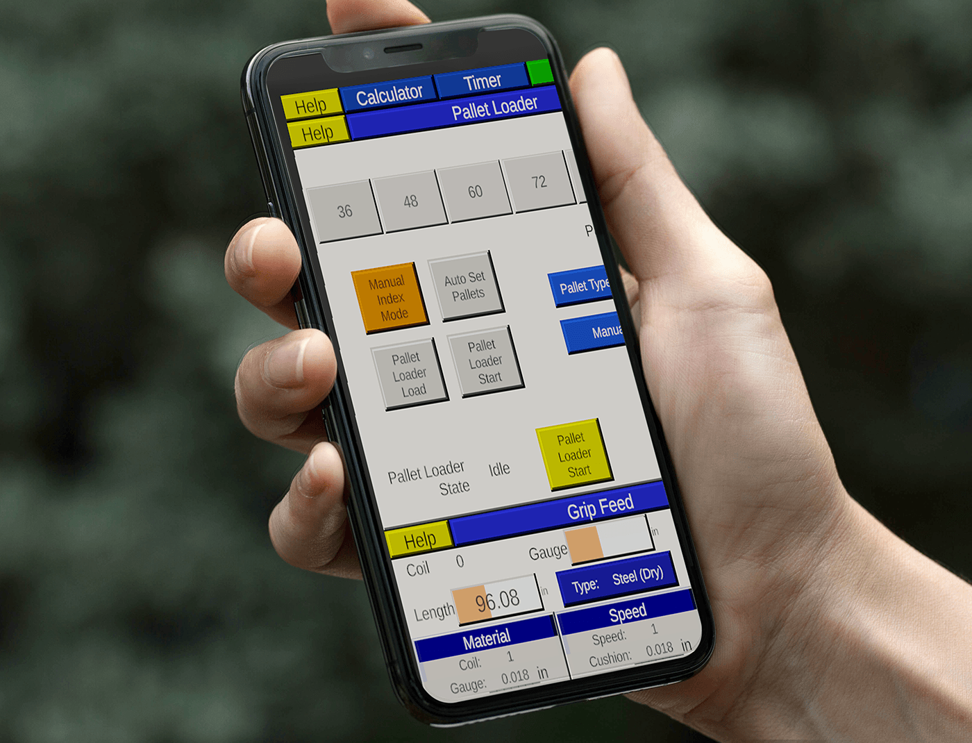 Designing Digitally - A person holds a smartphone displaying a control interface for a pallet loader, used in steel manufacturing training simulations, with various buttons and settings, including Manual Index Mode, Auto Set Bales, and Grip Feed. Designing Digitally -
