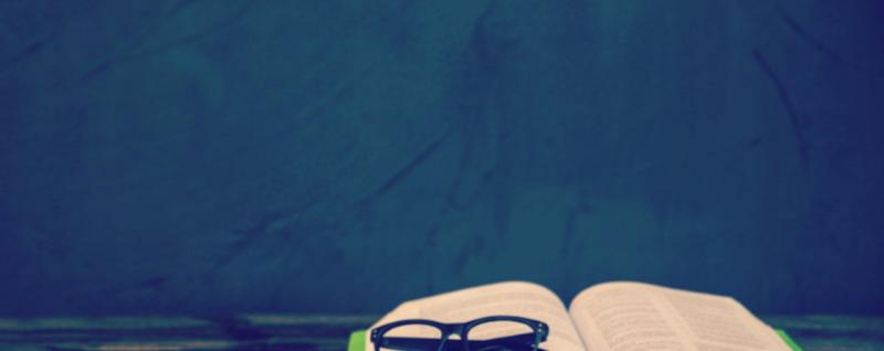 Designing Digitally - A pair of eyeglasses rests on an open book against a dark, textured background, illustrating the crucial connection between learner engagement and immersive study materials. Designing Digitally -