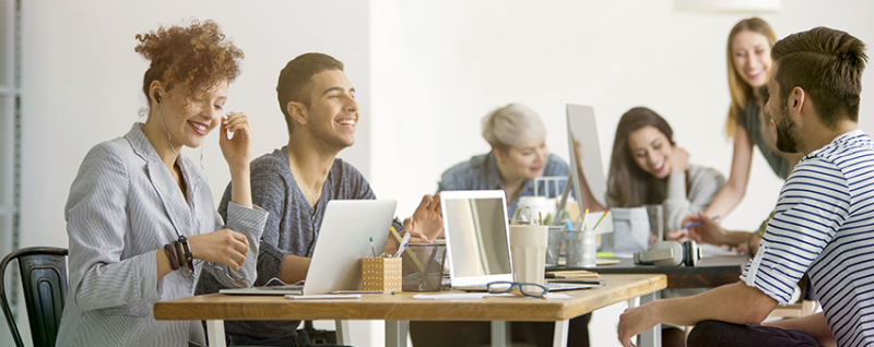 Designing Digitally - A group of six people, including a key vendor, engage in a meeting around a table. Some use laptops and notebooks, and they appear to be in discussion about enhancing learner engagement. The environment is bright and modern. Designing Digitally -