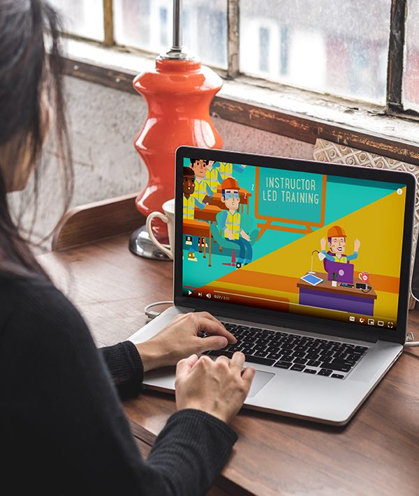 Designing Digitally - A person watches an "Instructor Led Training" video on a laptop at a desk with a red lamp by the window, incorporating training games for employee training to make learning engaging and interactive. Designing Digitally -